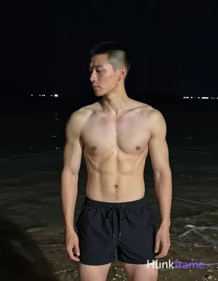 Asian man with short buzz cut and clean-shaven face stands upright in night beac