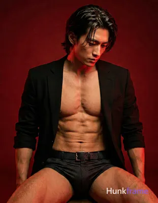 Adult man seated in a moody studio with solid red backdrop, shirtless under an o