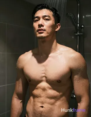 Asian adult man posing suggestively under shower spray Shirtless torso angled slightly toward camera