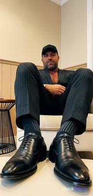 Adult man seated with legs extended forward, feet resting on a light-colored sur