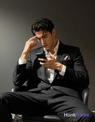 He sits on a black chair, leaning forward while his left hand touches the right 