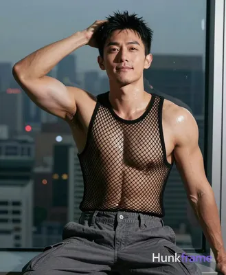 Asian adult man seated on edge of surface near window with city skyline visible 