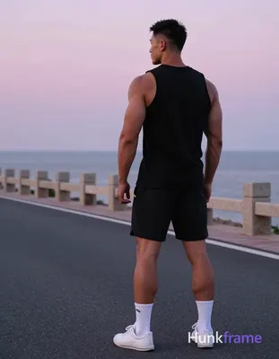 A muscular adult man stands full-body from behind on a coastal paved road at dusk, occupying the rig