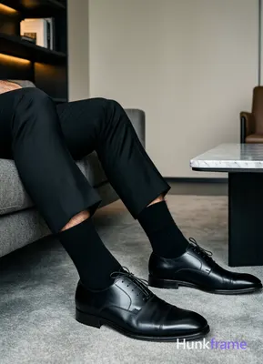 Seated adult man with thick thighs, legs extended forward slightly apart on a grey upholstered surfa