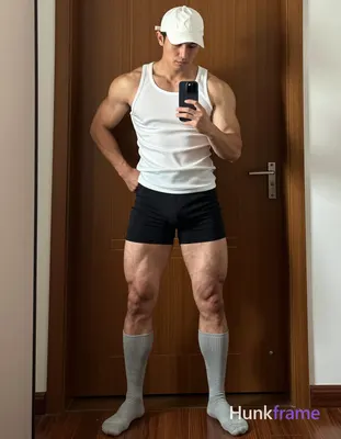 An adult masculine man with short dark hair under a white cap stands in a wide stance against an ind
