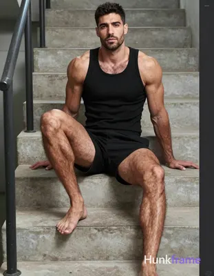 Vertical mid-shot of a very muscular man seated on concrete stairs, torso uprigh