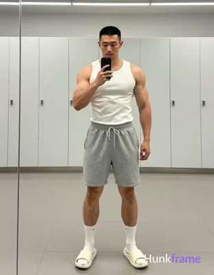 Asian man with short black buzz cut and light stubble stands full-body in front of a large mirror, f
