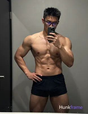 A shirtless muscular man taking a mirror selfie with one hand on his hip and the