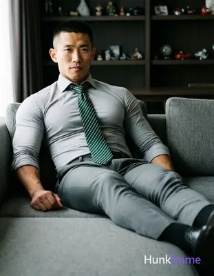 Asian man with short buzz cut and clean-shaven face reclining on a gray sectiona
