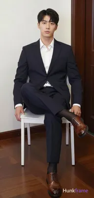 Adult man seated on a white chair, legs spread apart with right leg crossed over left knee, torso up
