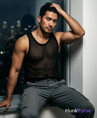 Asian man seated on edge of surface near window, left arm extended downward out 