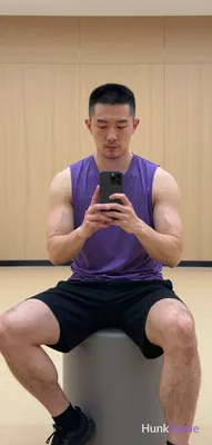 Asian man with short black buzz cut and light stubble sits centered in a gym mirror reflection on a 