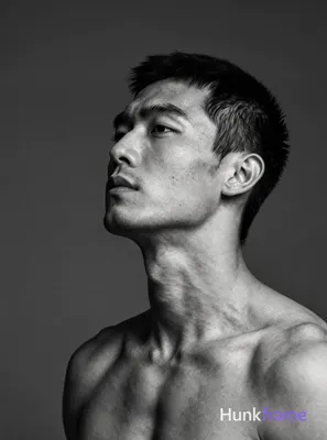 A handsome Asian man with a short black buzz cut and light stubble gazes upward 