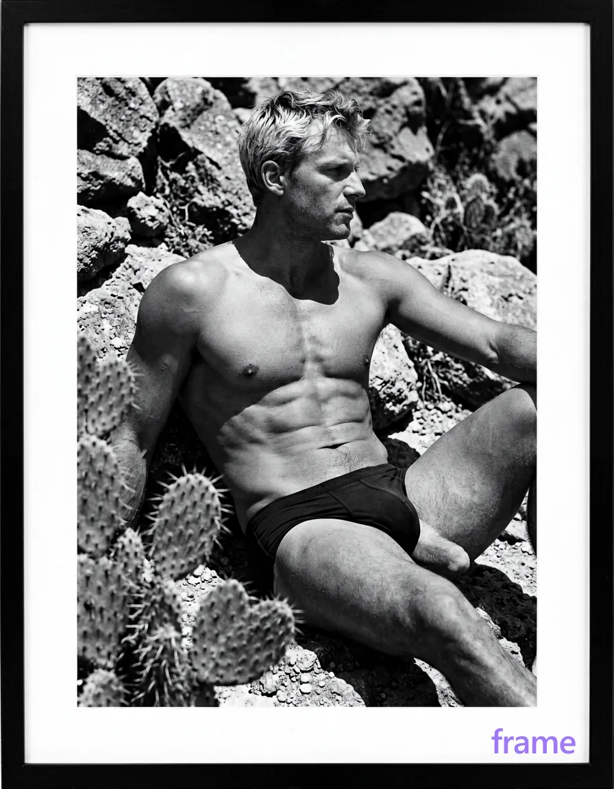 A lean white man with short light-colored hair sits contemplatively on rocky ground, torso turned slightly rightward. He is shirtless exposing his chest and abdomen in dark shorts partially obscured by a foreground cactus cluster. Natural daylight casts high-contrast sculptural shadows across the rugged terrain. The composition shifts to a tighter mid-frame crop focusing intensely on the upper body tension against the monochrome palette of black-and-white fine-art photography, framed within white matting inside a black border., same aesthetic theme and photo feel as the reference but a different man in a different pose with distinct body proportions, Mediterranean Italian man, olive skin, wavy dark hair, lean surfer body, wearing underwear or swim trunks, covered genitals, no frontal nudity, a single uninterrupted photograph only, no written words or typography anywhere in frame, no captions, no app UI, no social-media post layout, no screenshot borders