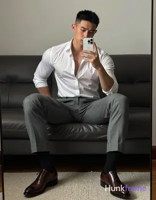 Asian man seated on dark leather sofa, legs spread knees bent taking mirror self