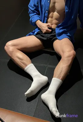 Adult man seated on black rubber gym flooring, legs extended forward with knees slightly bent; right