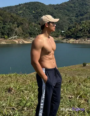 Adult man standing in profile facing right on a grassy hillside, left hand deep in pocket of dark na