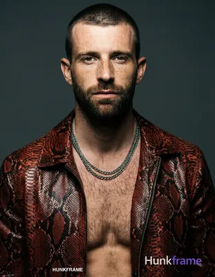 A fair-skinned white man with freckles and short dark cropped hair stands shirtless in a head-and-sh