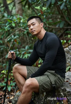 Asian man medium-tan skin short black buzz cut styled top light stubble seated on rock in forest tor