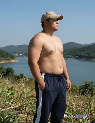 A big hairy stocky adult man stands in profile facing right on a grassy hillside left hand in pocket