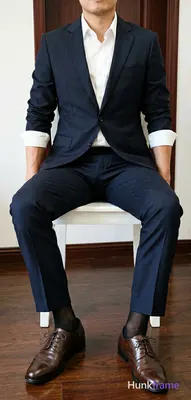 Adult man seated on a white chair, legs spread apart with right leg crossed over left knee, torso up