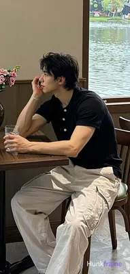 seated sideways at a dark wooden table; He wears a black short-sleeved polo shir