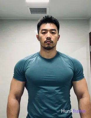 Asian man with short black textured hair and stubble beard stands facing camera 