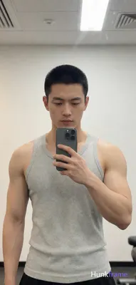 Asian man with short black buzz cut and light stubble on upper lip stands in gym mirror reflection h