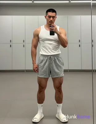 Asian man with short black buzz cut and light stubble stands full-body in front of a large mirror, f