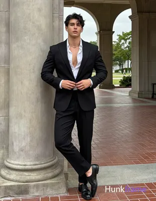buttoning white dress shirt under black suit jacket while leaning against stone column; Weight shift