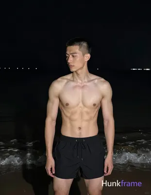 Asian man with short buzz cut and clean-shaven face stands upright in night beach setting, torso ang