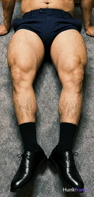 Seated man with thick thighs, legs extended forward slightly apart on gray textu