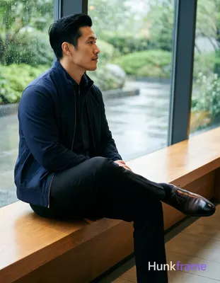 Asian man with fair skin and black short hair styled back sits sideways on a low
