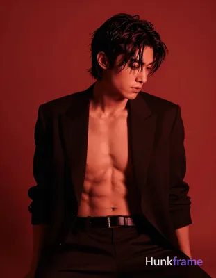 Adult man seated in a moody studio with solid red backdrop, shirtless under an o