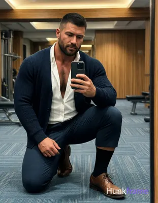 A rugged muscle bear with medium-brown skin and a black buzz cut kneels on blue-