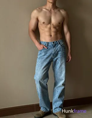 A handsome, muscular man leaning against a wall with one arm resting on it and the other hand in his