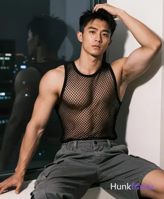 Asian man seated on edge of surface near window, left arm extended downward out 