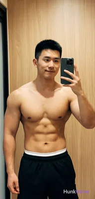 Asian muscular man with short black hair and clean-shaven face stands centered in a mirror selfie po