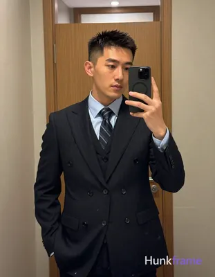 Asian man with short textured dark crop hair and clean-shaven face stands upright in a mirror reflec