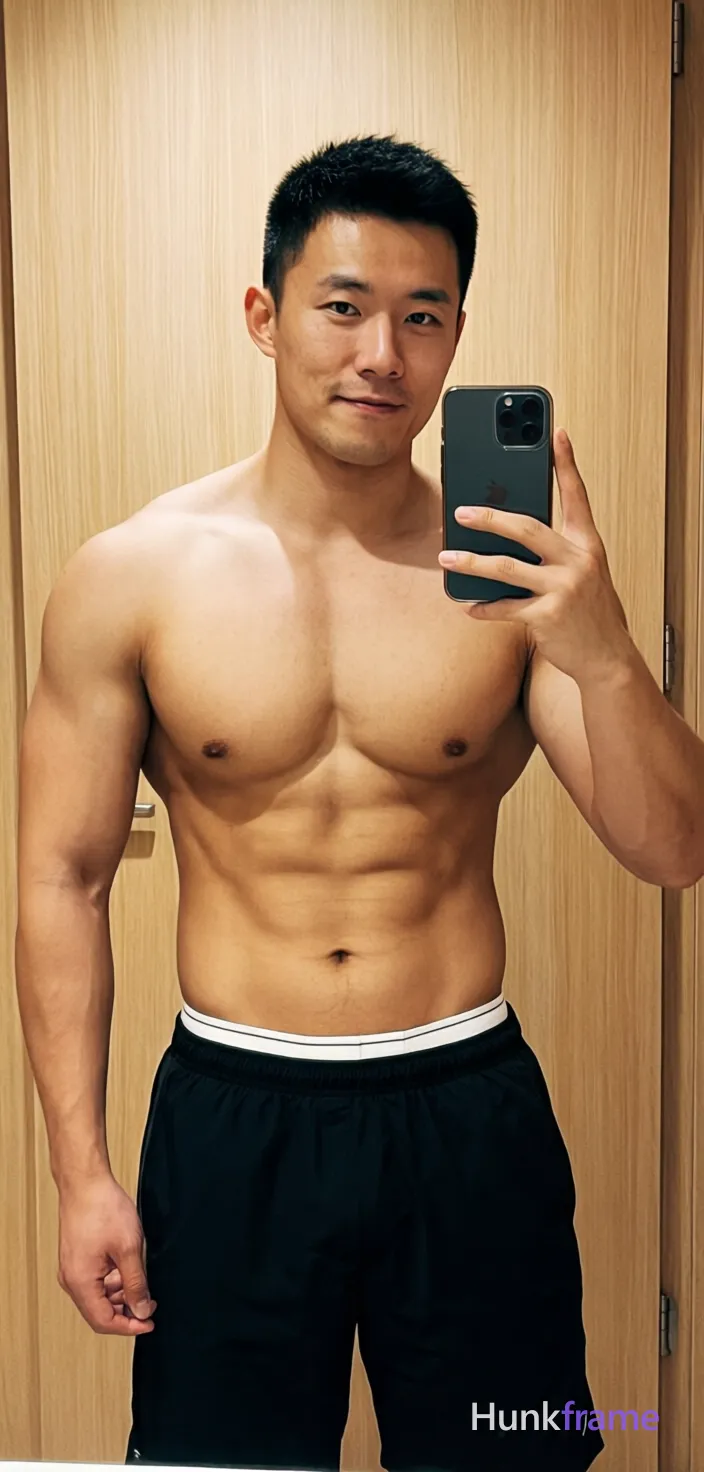 Asian muscular man with short black hair and clean-shaven face stands centered in a mirror selfie pose, holding dark smartphone right hand. Shirtless bare chest abdomen defined abs broad shoulders wearing black athletic shorts waistband visible white underwear waistband partially obscured. Indoor room light wood-paneled wall background warm indoor lighting neutral palette black white brown. Vertical portrait 13:19 aspect ratio full-body head to mid-thighs centered composition confident casual mood mirror selfie aesthetic social media post style., shot on iPhone 15 Pro main camera, authentic smartphone computational photography, natural Smart HDR and true-to-life skin texture, vertical 9:16 Xiaohongshu lifestyle feed, bright clean everyday scene, unretouched phone photo with subtle sensor grain, trendy Chinese internet 网红 aesthetic, candid influencer energy, phone held naturally in one hand for selfie, phone visible in frame