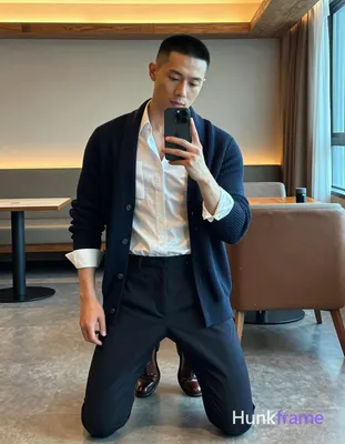 A handsome adult man with medium-brown skin and a black buzz cut stands in a trendy hotel lounge, ho