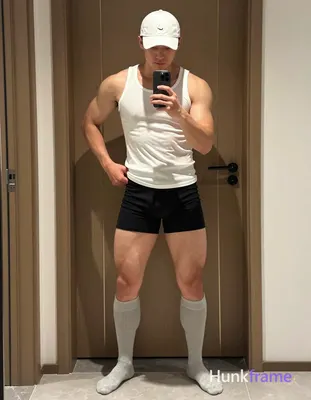 An adult masculine man with short dark hair under a white cap stands in a wide stance against an ind