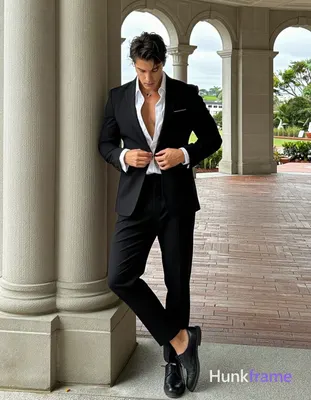 buttoning white dress shirt under black suit jacket while leaning against stone column; Weight shift
