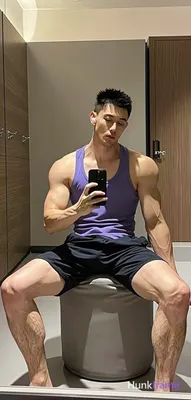 Asian man with short black buzz cut and light stubble sits on a cylindrical ottoman in a gym locker 