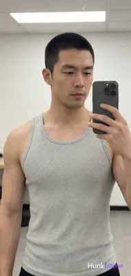 Asian man with short black buzz cut and light stubble stands in a gym interior, holding phone for mi