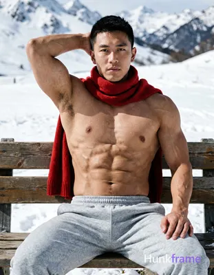 Asian man with short black hair and clean-shaven face seated on a wooden bench in an outdoor snowy m