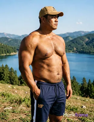 A big hairy stocky adult man stands in profile facing right on a grassy hillside left hand in pocket