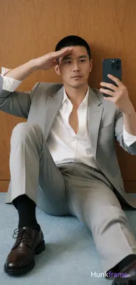 Asian adult man with short black buzz cut and light stubble, neutral expression saluting his forehea
