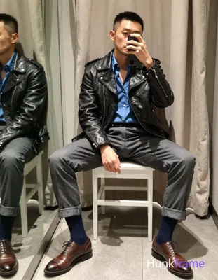 Asian man with short black buzz cut and light stubble sits on a white stool in an indoor dressing ro