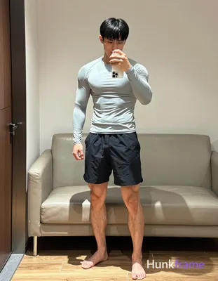 Asian man with short black hair and straight bangs stands in a modern dressing room, slightly turned